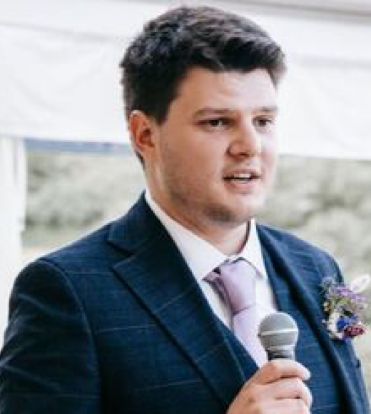 Man with brown hair wearing a suit and holding a microphone