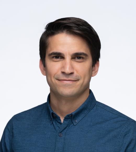 A person with short, dark brown hair wearing a blue button up shirt