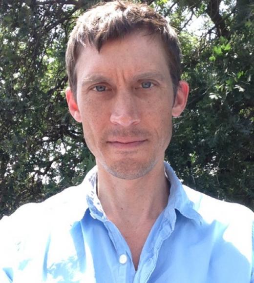 A man with short brown hair wearing a blue button up shirt