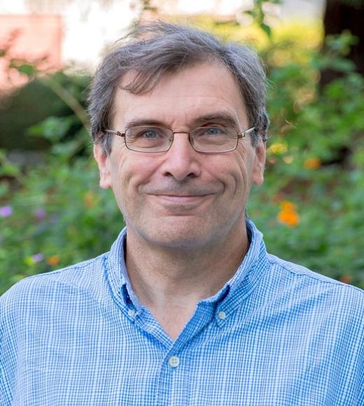 Man with grey hair and glasses wearing a blue button-up shirt