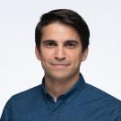 A person with short, dark brown hair wearing a blue button up shirt