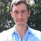 A man with short brown hair wearing a blue button up shirt