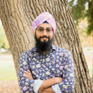 A man with a floral blue shirt and a pink turban stands in front of a tree